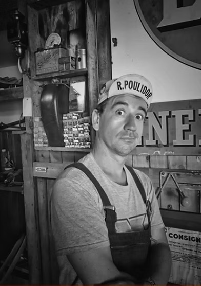 Portrait de Jonas dans son atelier, en casquette de cycliste et salopette